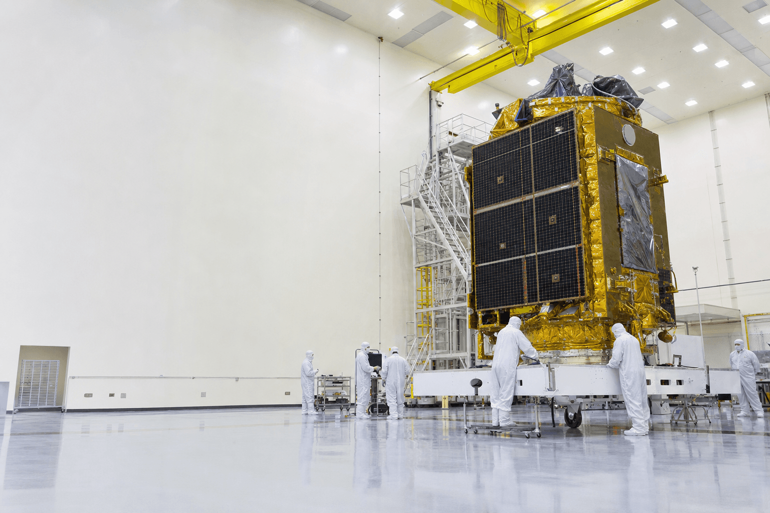 Engineers in white cleanroom suits working around a gold-foil-wrapped satellite inside a spacecraft integration hall.